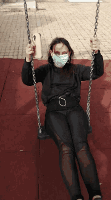 a woman wearing a mask is swinging on a chain