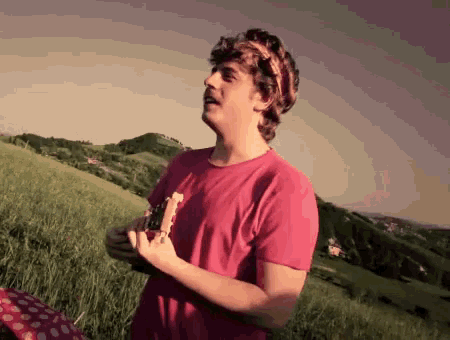 a young man in a pink shirt is standing in a field