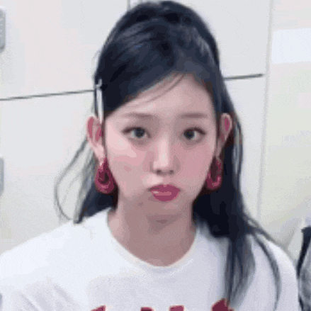 a close up of a girl wearing a white shirt and red earrings .