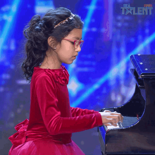 a little girl in a red dress is playing a piano in front of a blue background that says " esta talent "
