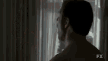 a man without a shirt is standing in front of a window .