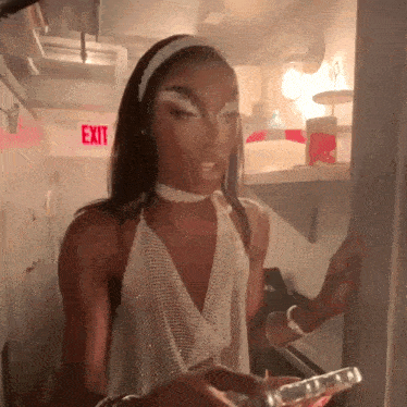 a woman in a white dress is standing in front of an exit sign