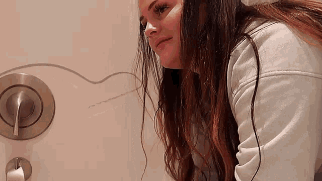 a woman in a white sweatshirt is sitting in a bathroom next to a toilet