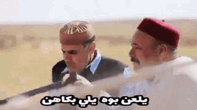 two men are standing next to each other in a field holding guns and talking in arabic .