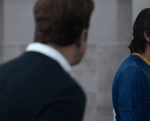 a man in a blue shirt is standing next to another man in a suit