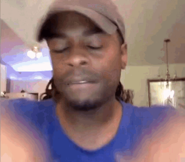 a man wearing a hat and a blue shirt is making a funny face with his eyes closed .