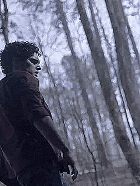 a man in a red shirt is standing in a forest with trees in the background