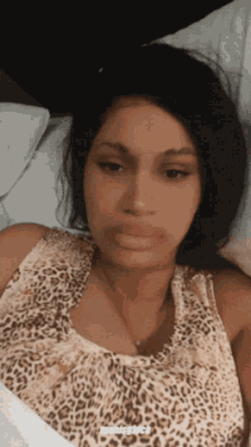 a woman wearing a leopard print tank top is laying in bed