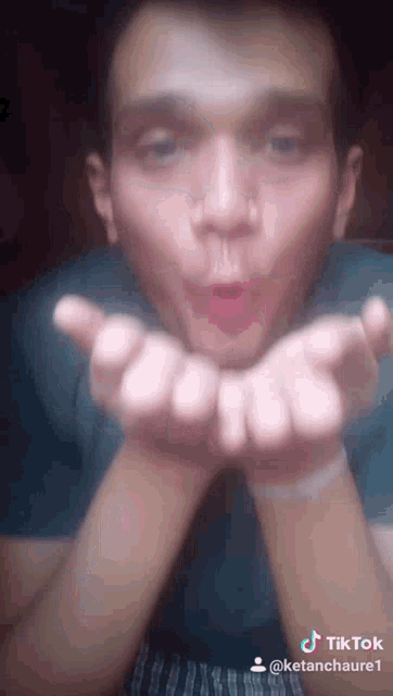 a man is blowing a kiss with his hands in front of his face .
