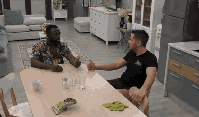 two men sitting at a table with a bag of chips on it