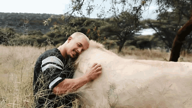 a man in a black and white striped shirt is hugging a white horse