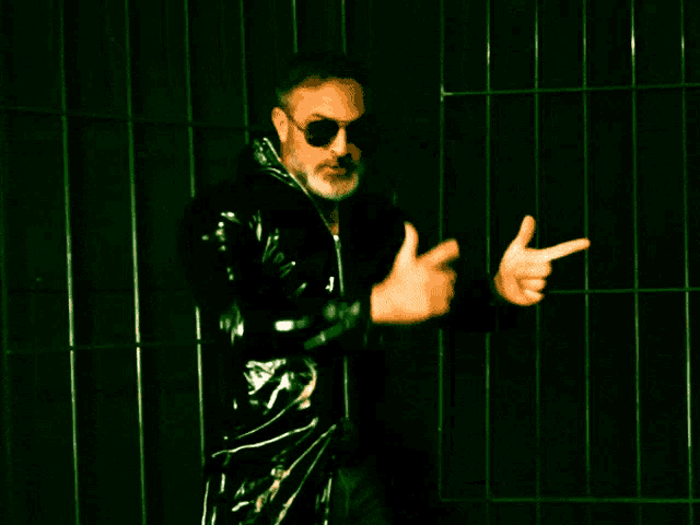 a man wearing sunglasses and a black leather jacket is pointing at the camera