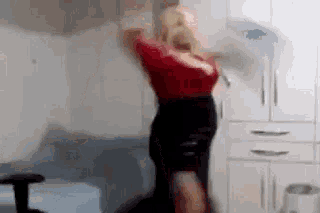 a woman in a red top and black skirt is dancing in a room with white cabinets .