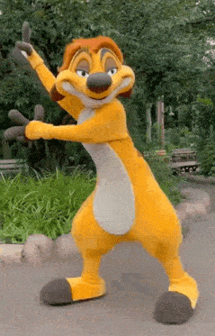 a mascot from the lion king is dancing in front of trees and giving a thumbs up .