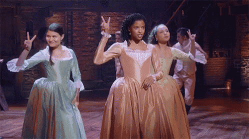 a group of women in dresses are standing next to each other on a stage giving the peace sign .