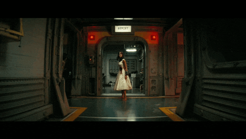 a woman in a white dress walking down a hallway with an exit sign