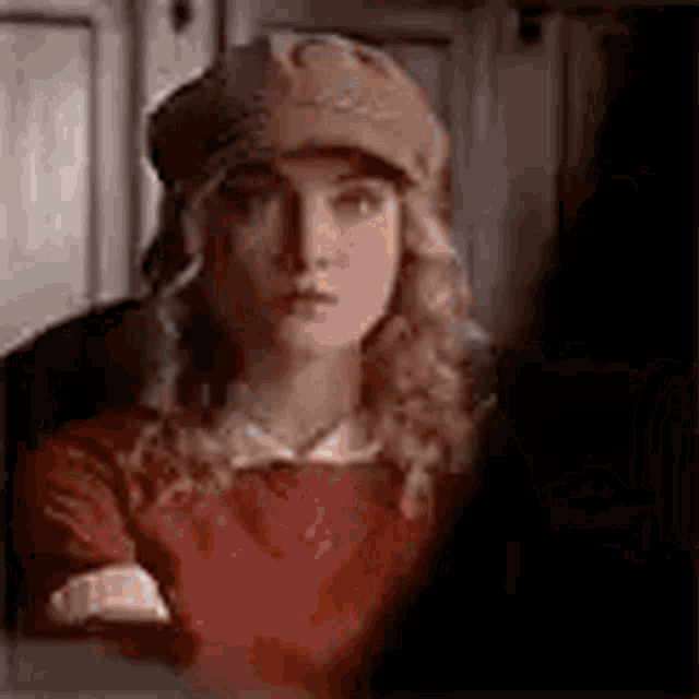 a woman wearing a hat and a red shirt is sitting in a dark room .