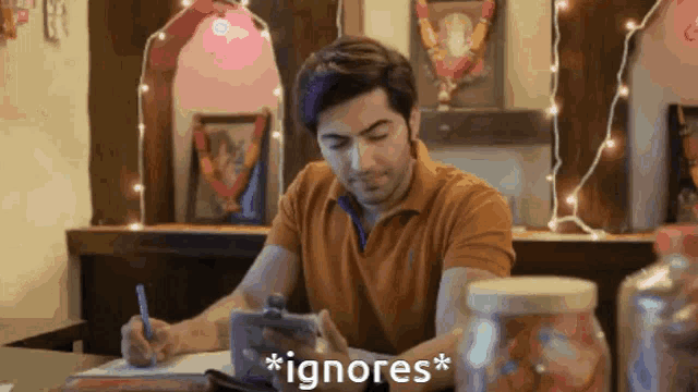 a man is sitting at a table looking at a cell phone and says " ignores "