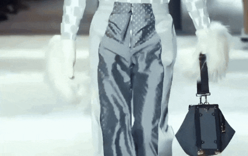 a woman is walking down a runway holding a purse .