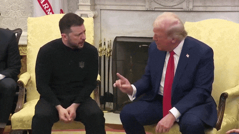 a man in a black shirt talks to a man in a suit and tie
