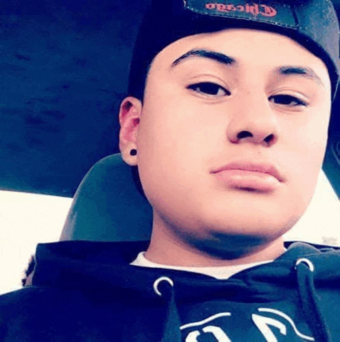 a young man wearing a black hat and a black hoodie is taking a selfie in a car .