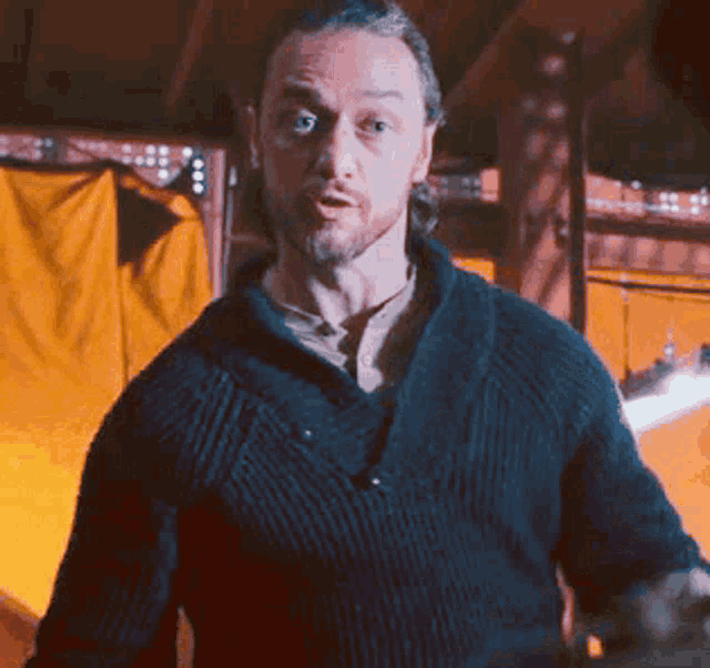 a man in a black sweater is standing in front of a yellow curtain