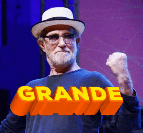 a man wearing a hat and glasses holds his fist up in front of a large orange sign that says grande
