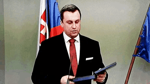 a man in a suit and tie is holding a piece of paper in front of a flag