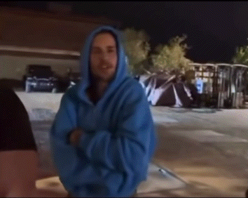 a man wearing a blue hoodie is standing in a parking lot