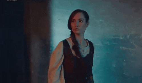 a woman in a medieval dress is standing in a dark room looking at the camera .