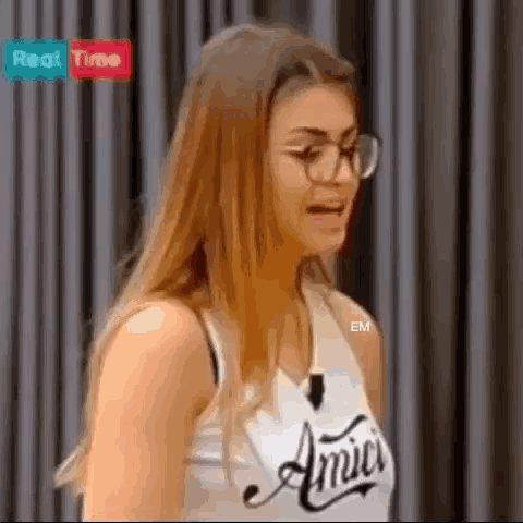 a woman wearing glasses and a white tank top with the word amici on it is making a funny face .