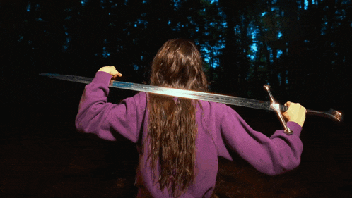 a woman in a purple shirt is holding a sword over her shoulder