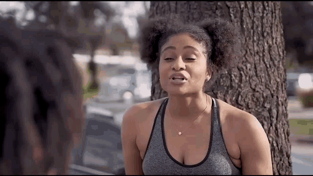 a woman in a sports bra is standing next to a tree .