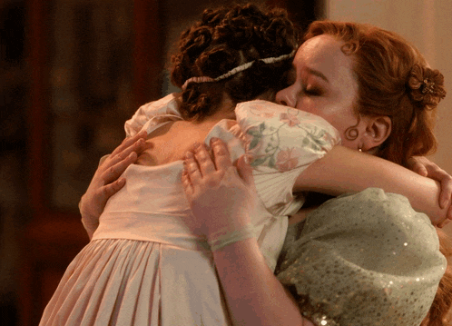 a woman in a white dress is hugging another woman with red hair