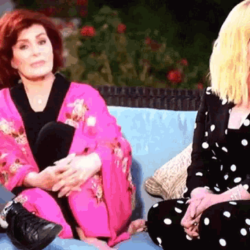 two women are sitting on a blue couch one is wearing a pink kimono and the other is wearing polka dot pants