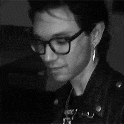 a man wearing glasses and earrings is looking at the camera in a black and white photo