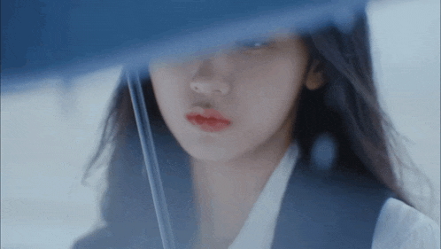a close up of a woman 's face behind a blue umbrella .