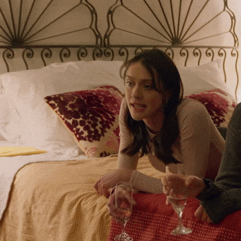 a woman sits on a bed with a glass of wine in her hand