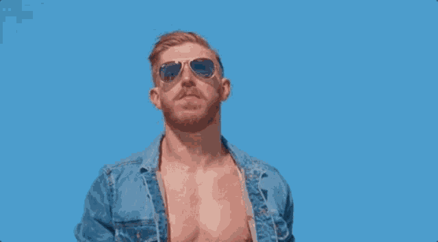 a shirtless man in a denim shirt is standing on a beach .