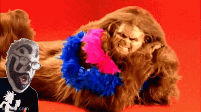 a man with glasses is laying next to a furry monster with a feather boa around his neck