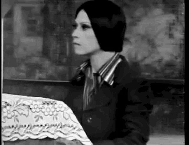 a black and white photo of a woman sitting at a table with a tablecloth .