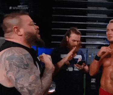 a man with a tattoo on his arm is talking to another man while another man holds a cell phone