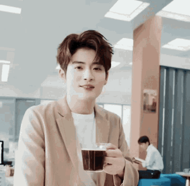 a young man in a tan jacket is holding a cup of coffee in his hand .