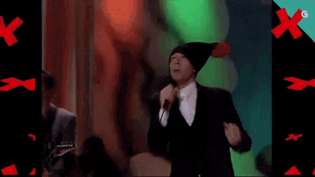 a man singing into a microphone while wearing a black hat with red pom poms