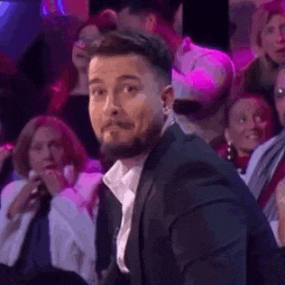a man in a suit is sitting in a crowd of people and making a face .