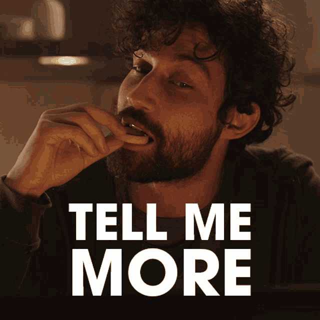 a man with a beard is eating a cookie and the words tell me more are behind him