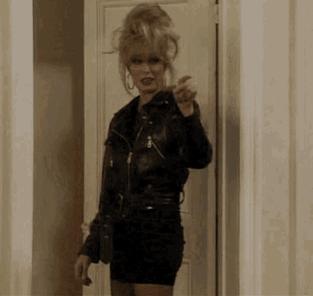 a woman wearing a leather jacket and a black dress is standing in a doorway .