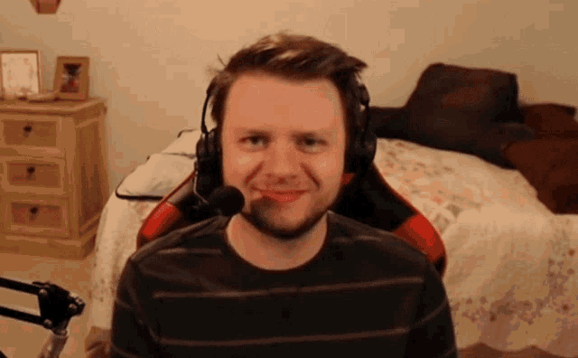 a man wearing headphones and a microphone smiles in front of a bed