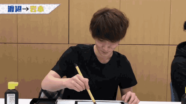 a man in a black shirt is writing on a piece of paper with a brush