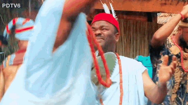 a man wearing a red hat and a necklace is dancing in front of a sign that says pdtv6 on it